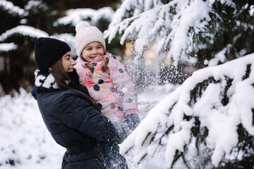 Happy mom and daughter shake off the snow from a Christmas tree branch