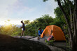 Teenager Travelers Pitch Vibrant Orange Tent on Cliff with a Natural View, Embracing Pristine Natural Views or Surrounded by Cliffside Beauty, an Unforgettable Camping Journey.