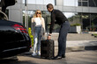 © rh2010 - Chauffeur packs a suitcase in a car trunk, businesswoman waiting nearby using luxury taxi service during a business trip. Concept of business transfer services, idea of personal driver.