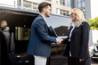 Female chauffeur greets the businessman while helping him to get out of the minivan taxi. Concept of personal driver, luxury taxi for business people