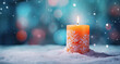 vela de navidad decorada y encendida sobre superficie nevada  y fondo desenfocado en tono azul