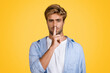 © Prostock-studio - Serious european man gesturing silence on yellow backdrop