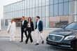 © rh2010 - Group of business people talking on the go from modern building of airport or some office to luxury taxi on parking lot on sunset. Business partners are going to leave by luxury car