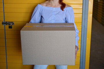 Woman stands with a cardboard box near a yellow door