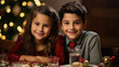 Two cheerful children, a boy and a girl, possibly siblings, sitting at a dinner table with a festive Christmas tree in the background, smiling warmly at the camera.