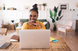 © BullRun - Smiling black woman sitting at table with laptop