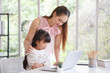 © aekkorn - Children education and home school concept : Young asian mother pleased to see little daughters' study online. Excited smiling child girl enjoying online learning  with pleasant mom at home.