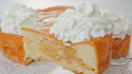 Slice of a freshly baked apple cake with whipped cream topping. Chef serving a cake