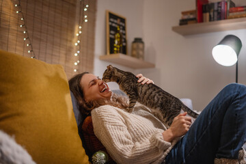 Cozy at home with tabby cat, woman with her pet on sofa ay home in evening