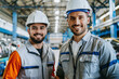 Zwei junge Männer Facharbeiter/Fachkräfte in Arbeitskleidung und Helmen lächelnd in einer Industriehalle