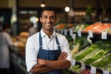 Fototapeta  - Portrait of a handsome seller with arm crossed in supermarket. Portrait of smiling man wearing apron at supermarket