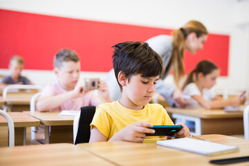 Wall Mural - Young boys and girls using their smartphones during lesson