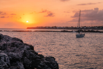 Wall Mural - View of the sunset over the mediterranean sea and the southern coast of Menorca/Minorca in the Balearic Islands (Spain), from the rocky shores, with a sailboat in the foreground.