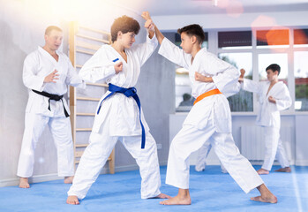 Wall Mural - Concentrated teen boys in kimonos honing punching techniques during kumite at karate training session under guidance of sensei..