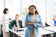 © BullRun - Confident black woman with crossed arms in office together with coworkers