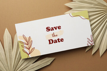 Wall Mural - Beautiful card with Save the Date phrase and leaves on beige background, top view