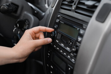 Wall Mural - Listening to radio while driving. Woman turning volume button on vehicle audio in car, closeup