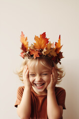 Wall Mural - portrait of a joyful smiling child wearing a fall autumn crown wreath made of leaves for thanksgiving craft