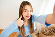 © Monster Ztudio - Pretty young asian female with big smile sitting at living room. She having fun taking light cheerful selfie on blurred background
