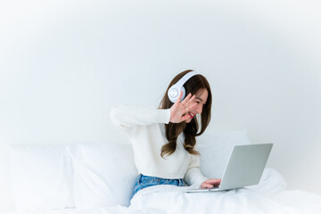 Wall Mural - Morning Time in Bedroom Young Asian Woman Happy Working on Computer Laptop, Wearing headset, Sitting on Bed at House