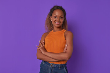 Wall Mural - Young successful confident African American business woman stands with arms crossed in front of chest and looks at screen with satisfied emotions inviting you to cooperate posing in purple studio.