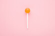 © fotoduets - Orange lollipop on stick on light pink table background. Pastel color. Sweet candy. Closeup. Top down view.
