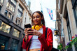 © Westend61 - Smiling woman with eyeglasses and headphones using mobile phone in city