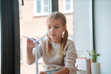 Blond Girl Playing With Wind Turbine Model In Window At Home