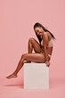 Beautiful, smiling young African woman with long hair posing in underwear against pink studio background. Multiethnic beauty. Concept of mixed beauty, feminisms, body acceptance, self-care