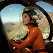 © soleg - Portrait of a woman dressed in a red latex suit, sitting inside a glass cabin of a futuristic transport and driving it