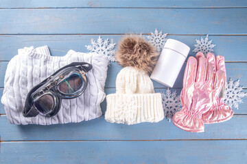 Winter sport and fitness, active lifestyle background. Warm knitted hat, sweater, jump rope, ski mask, thermal mug with hot tea, gloves, winter sneakers on wooden blue background, snowflakes, top view