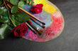 Artist's palette, brushes and red roses on a dark background.