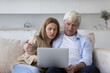 © fizkes - Overjoyed mature father and daughter excited with sport match online broadcasting, resting on couch with laptop, watching TV on Internet, smiling, laughing, shouting for joy, making winner hand