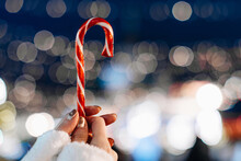 Female Hands Holding Red White Cane Sweet Candy Lollipop Against The Background Of Blue Silver Magic Illumination. Christmas Holiday Fairy Details