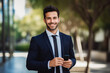 © VisualProduction - Business man smiling at the camera and holding a cellphone. Portrait of confident young man in a suit smiling at camera. Business concept.