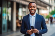 © VisualProduction - Business man smiling at the camera and holding a cellphone. Portrait of confident young man in a suit smiling at camera. Business concept.