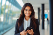 © VisualProduction - Indian business woman smiling at the camera and holding a cellphone. Portrait of confident young woman in a suit smiling at camera. Business concept.