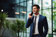 © VisualProduction - Indian business man smiling and holding cellphone, making a business call. Portrait of confident young man in suit smiling at camera. Business concept
