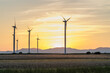 Erneuerbare und nachhaltige Energieerzeugung mit rotierenden Windrädern, abends im Gegenlicht auf freiem Feld 