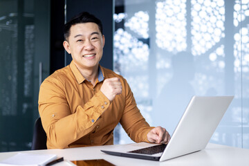 Wall Mural - Portrait of young successful asian man inside office at workplace, man smiling and looking at camera, using laptop at work, programmer entrepreneur developer in shirt.