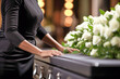 A woman is standing beside a casket with a bouquet of flowers on it.