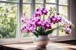 A bouquet of orchid and carnation flowers, placed in an elegant ivory ceramic vase, on a wooden surface, near an open window.
