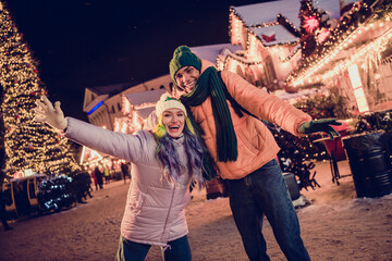 Canvas Print - Photo of cheerful impressed african guy lady dressed coats rising arms enjoying x-mas shopping together outdoors urban fair park