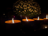 Fototapeta  - trzy ceramiczne znicze płonące na nagrobku stojące obok kwiecistej chryzantemy