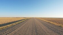 POV From The Front Of A Vehicle Driving Along A Gravel Road Through Open Prairie In The Fall. The Truck Slows To Cross A Texas Cattle Gate. The Sky Is Blue With Hazy White Clouds.
