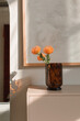 © Nina - Bright orange flowers in a glass vase on a wooden dresser in a modern interior in the rays of the sun.