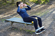 Young sporty athletic woman trains her abs with sit ups on an exercise bench outdoors in autumn 	