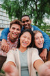 © Jose Calsina - Vertical portrait of a group of young multiracial high school students with a toothy smile taking a selfie outside looking at camera, laughing and having fun together. Friendly teens shooting a photo