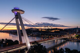The SNP bridge over the Danube river with night panorama of Bratislava with castle on the hill, Slovakia