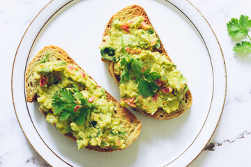 Toasts with guacamole on white plate on marble background.